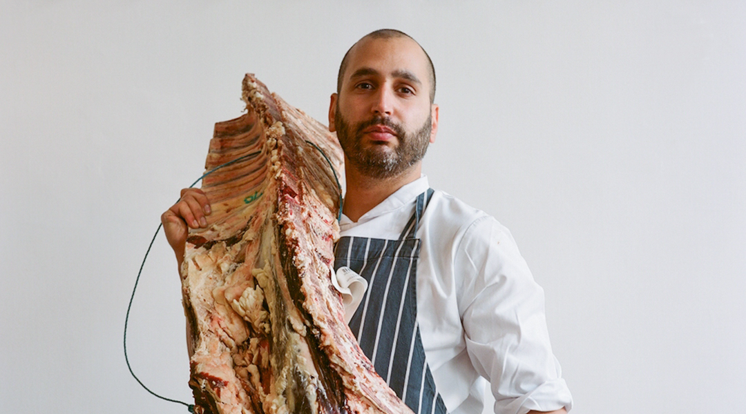 St. JOHN Bread & Wine chef Farokh Talati wearing chef whites and striped apron, holding an animal carcass