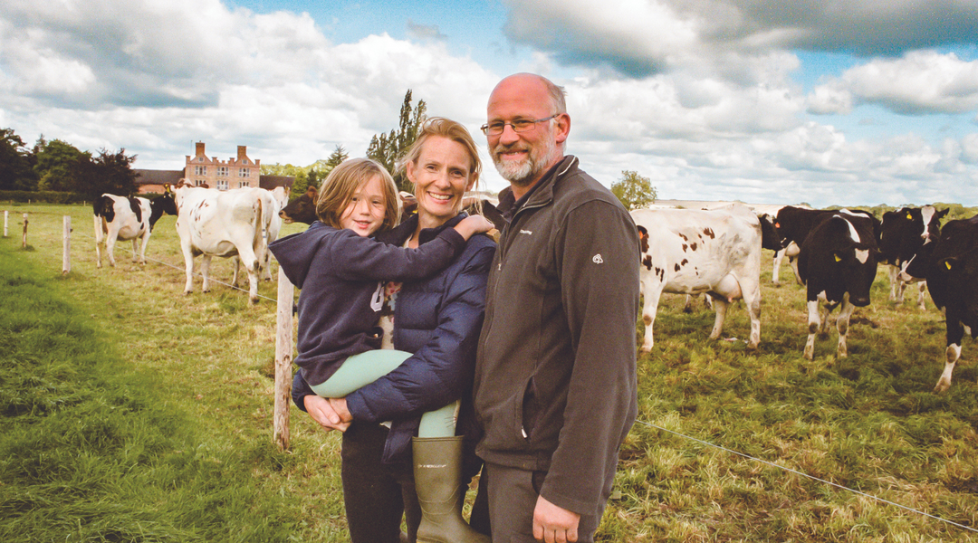 Sarah & Paul Appleby with their daughter in front of a field of cows© Harry Darby