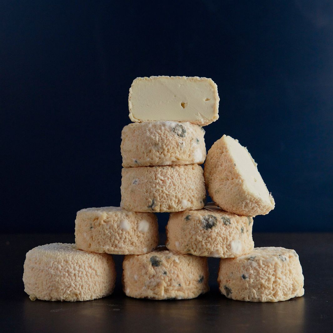 A pile of whole and cut Brefu Bach, showing the smooth mousse-like paste and mould spots forming on the outside of the cheese.