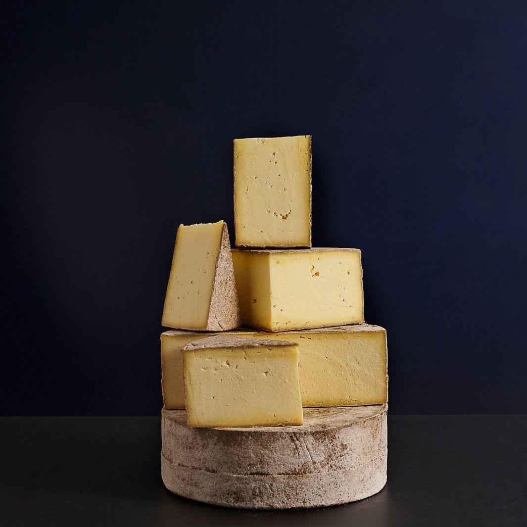 Various sized cut pieces sat on a whole Duckett’s Caerphilly raw cow’s milk cheese, showing the crumbly curd paste and edible natural rind