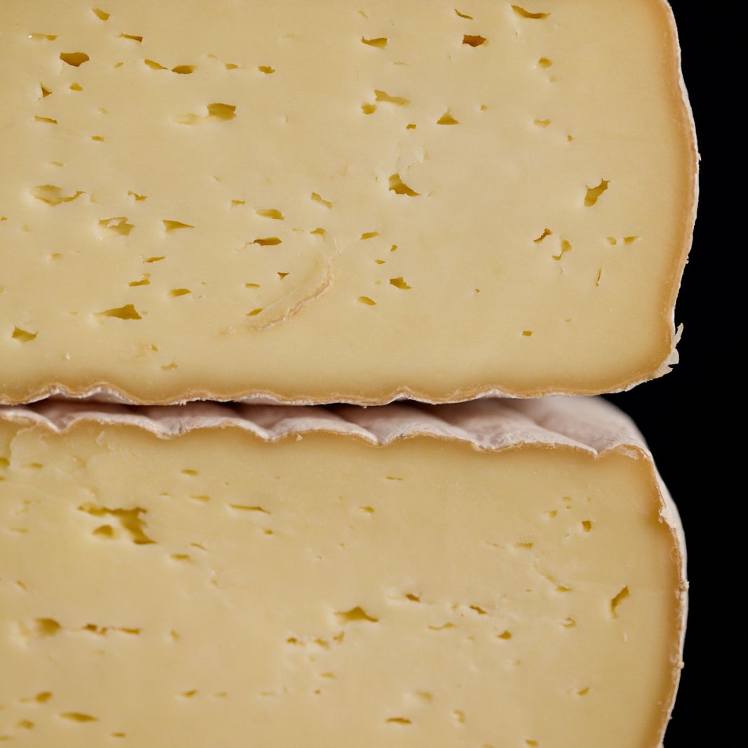 Cross-section of a whole Gubbeen semi-soft washed rind cow’s milk cheese, showing the patterned rind and creamy-coloured paste